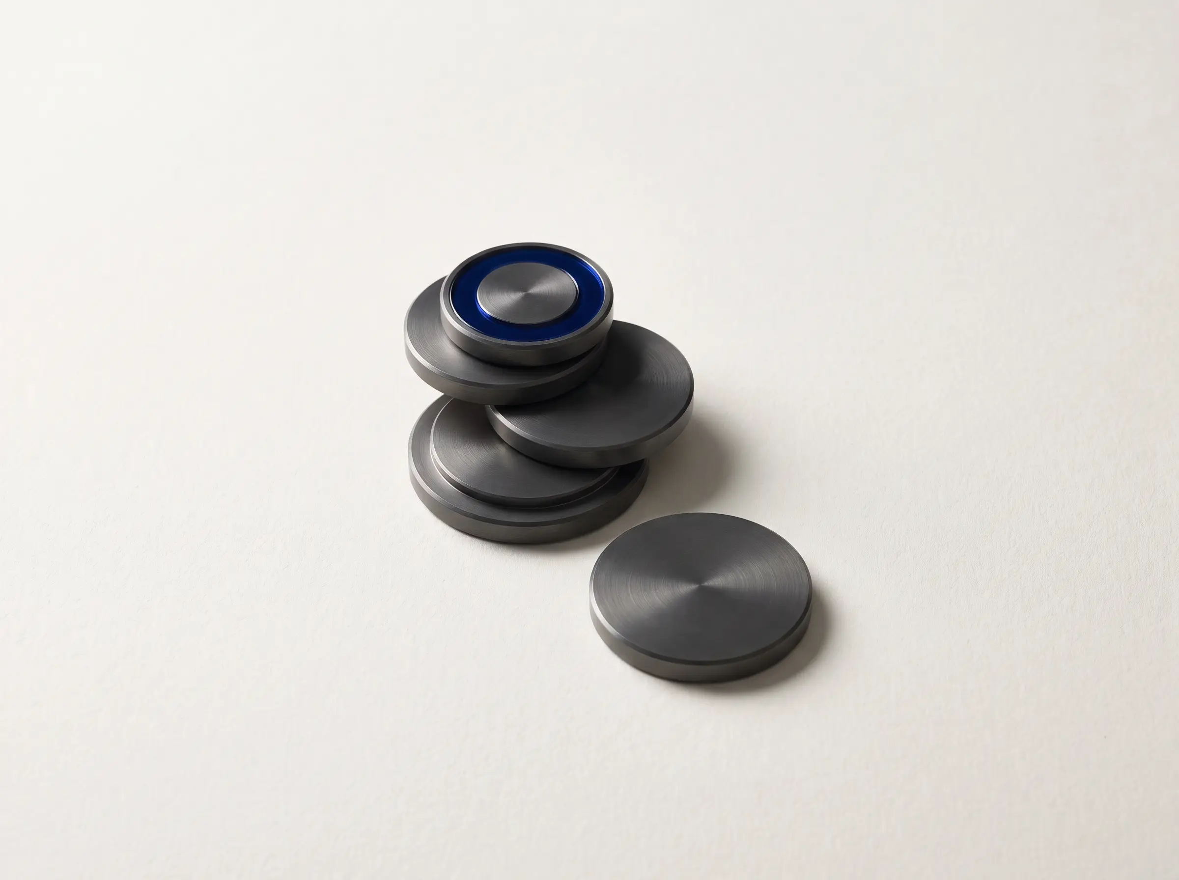 A descending stack of machined discs, the top one ringed in cobalt, representing turns spent before any work lands.